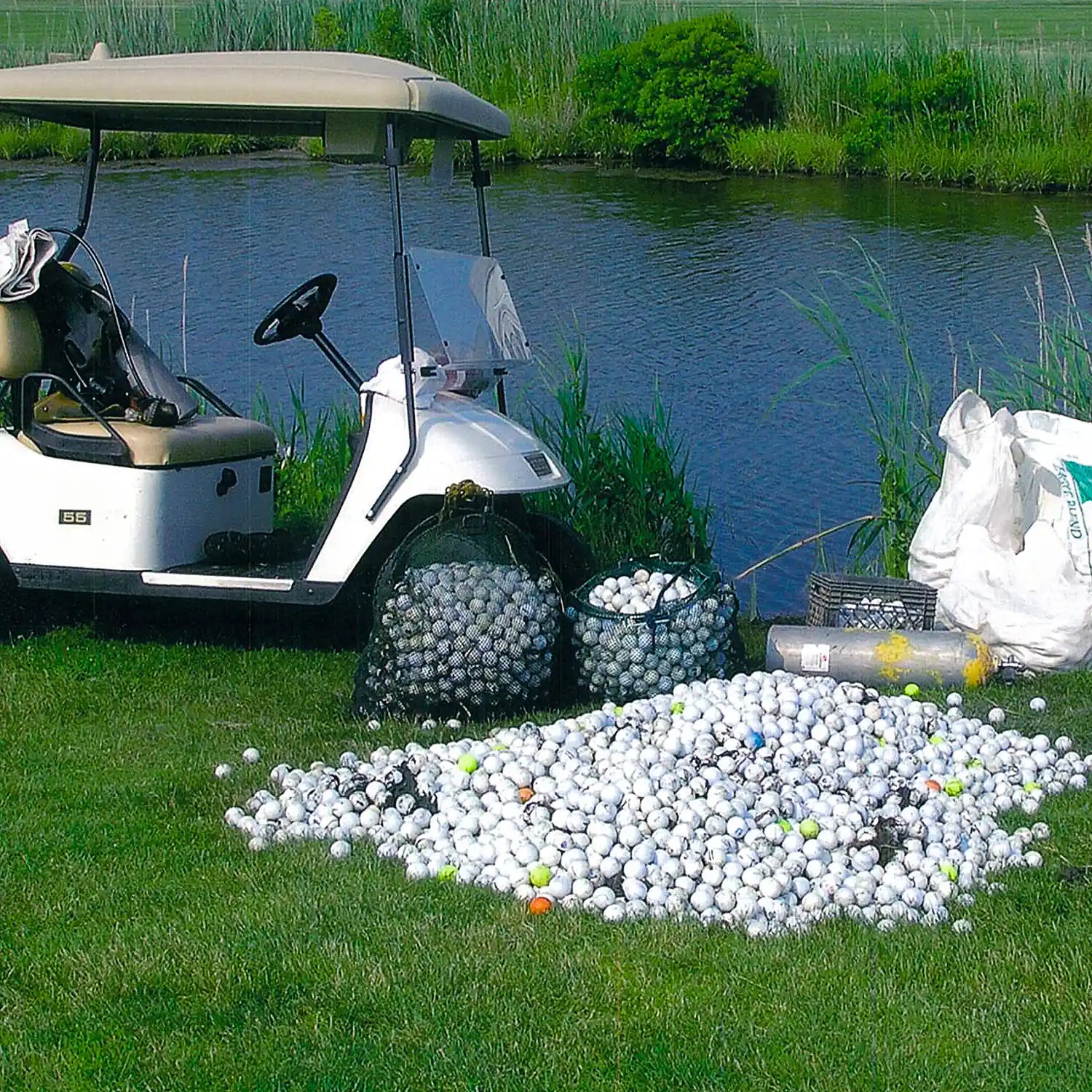 Golf cart with bags of golf balls near a body of water
